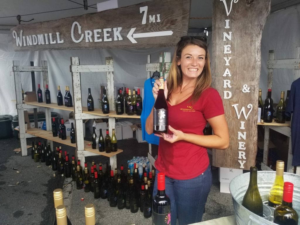 girl in red Windmill Creek shirt holding a bottle of red wine