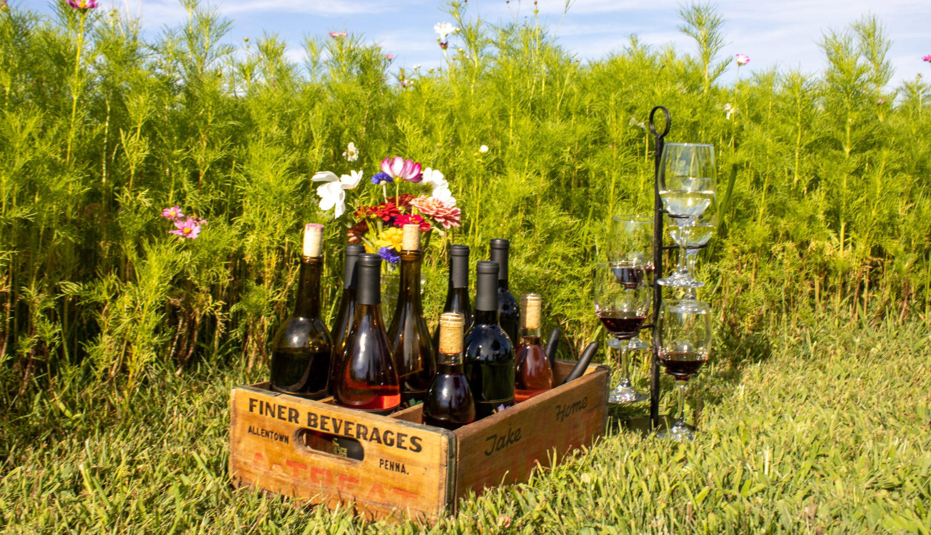 Case of wine next to multiple glasses in the field of flowers