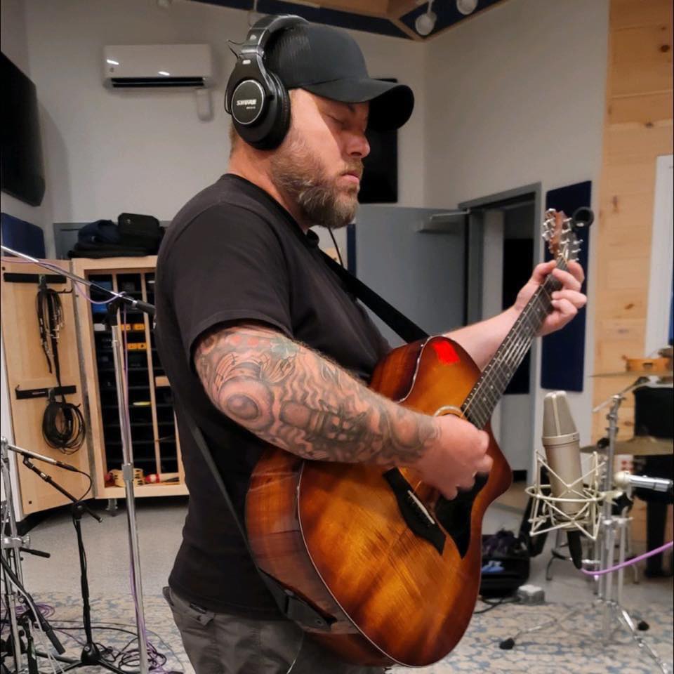 Picture of Dustin Showers playing guitar in studio with headphones.
