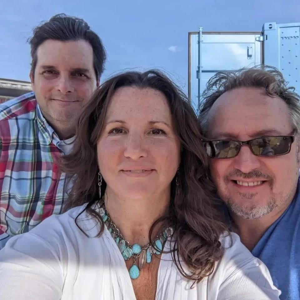 A woman with brown hair taking a picture with two men