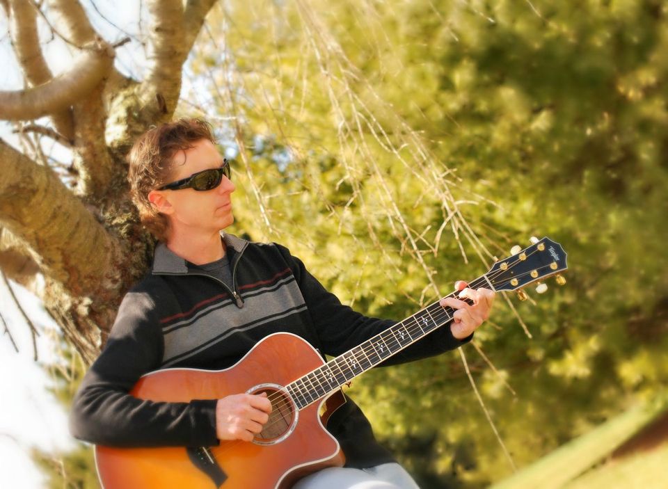 Man leaning against a tree playing the guitar