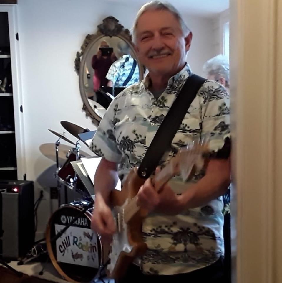 Man with button down shirt playing the guitar and smiling