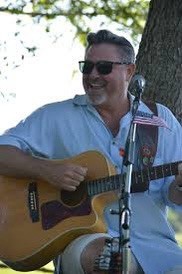 white man in a blue shirt strumming an acoustic guitar